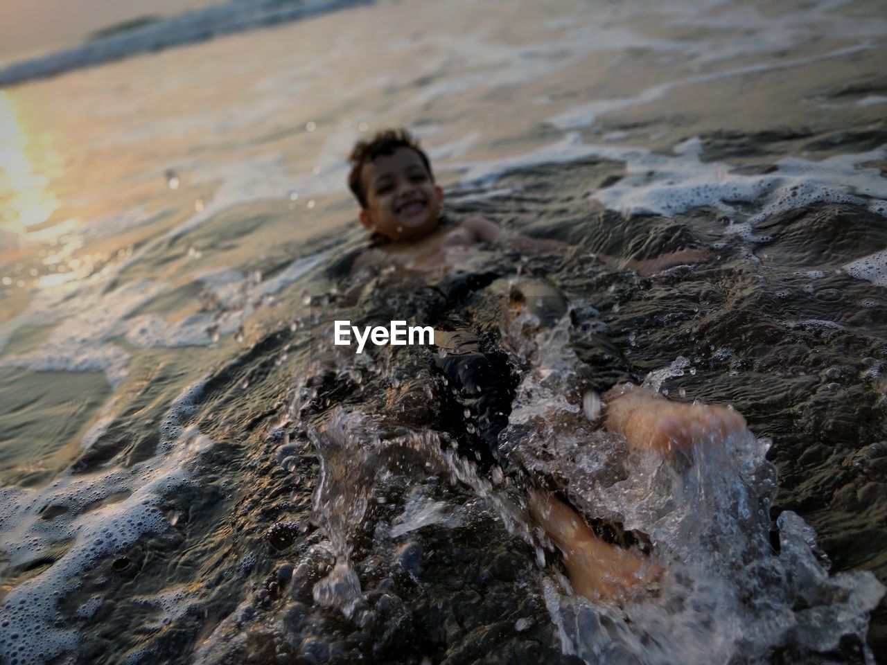 Shirtless boy swimming in sea during sunset
