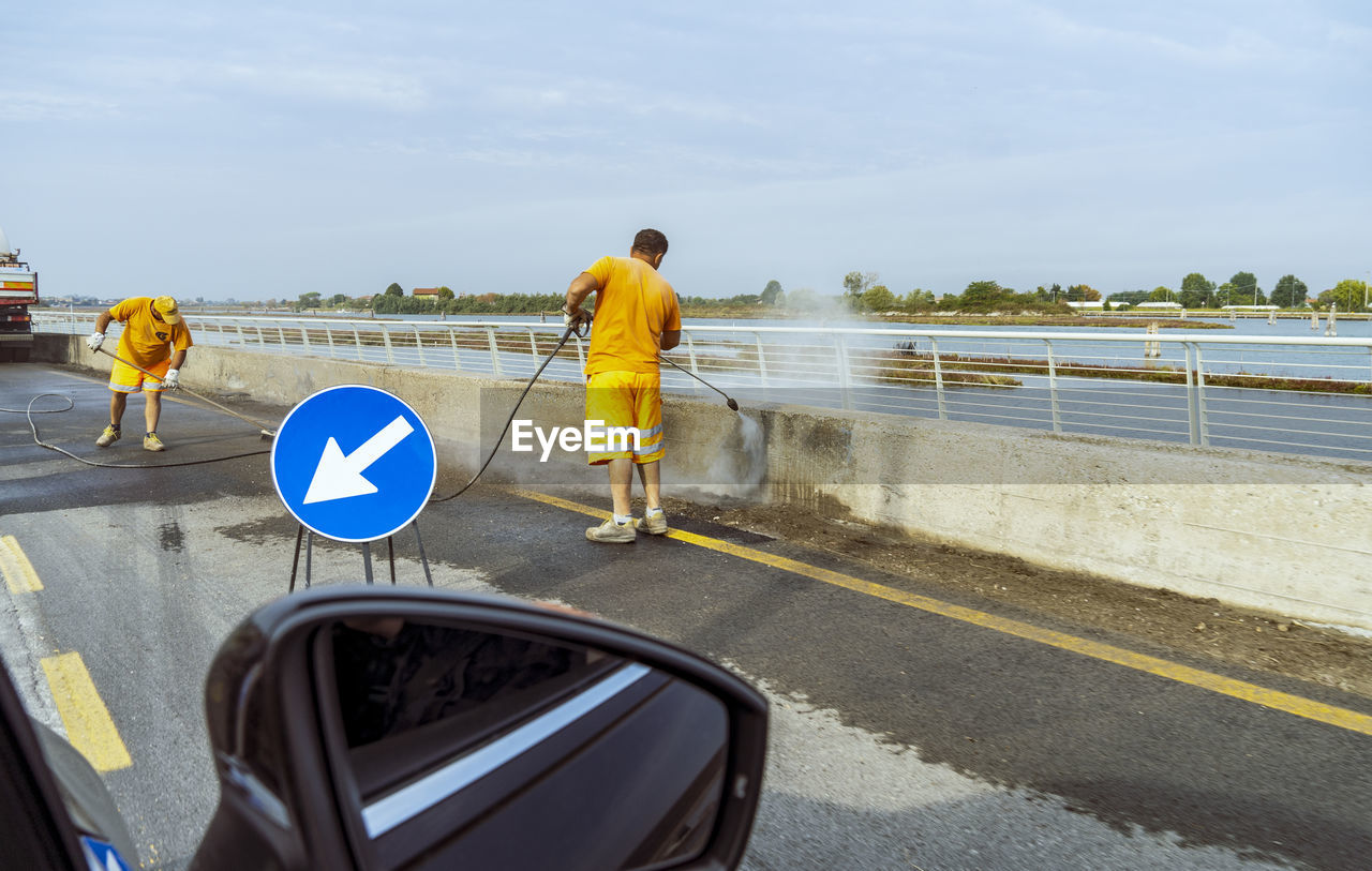 transportation, road, men, sign, day, one person, water, mode of transportation, adult, symbol, sky, full length, road sign, nature, road marking, communication, marking, motor vehicle, vehicle, outdoors, rear view, standing, land vehicle, travel, lifestyles, car, city, railing, person, sports