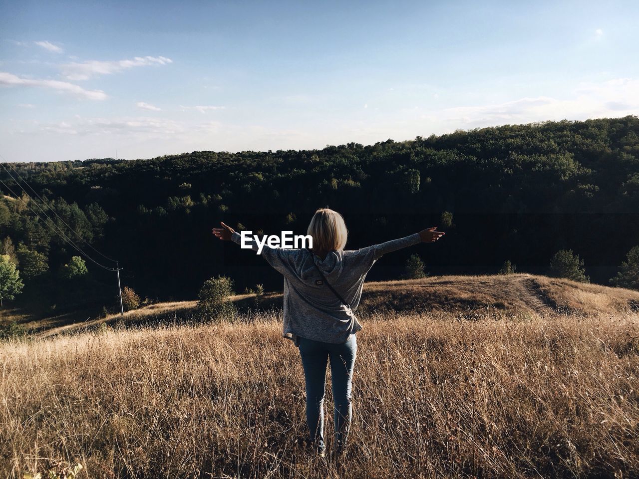 Rear view of woman with arms outstretched standing on grassy field against sky