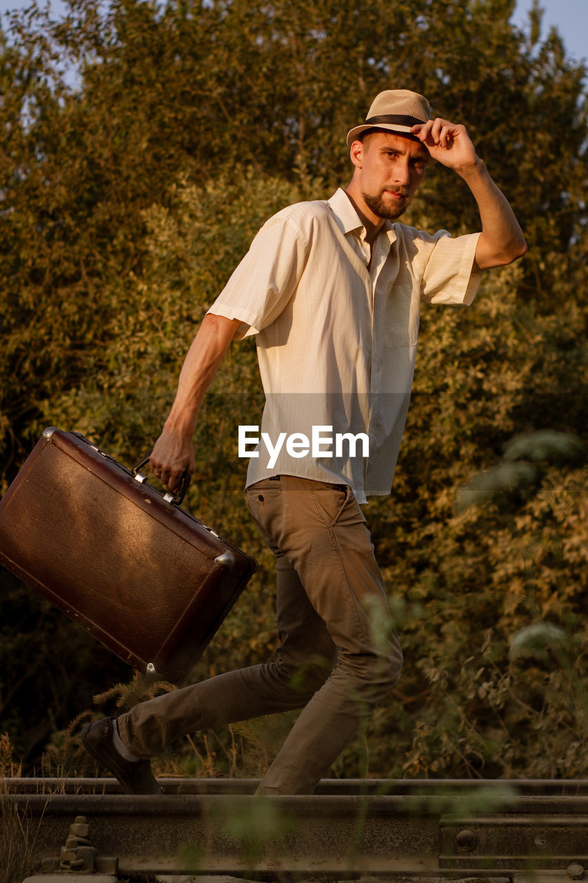 Portrait of young man holding suitcase running on track