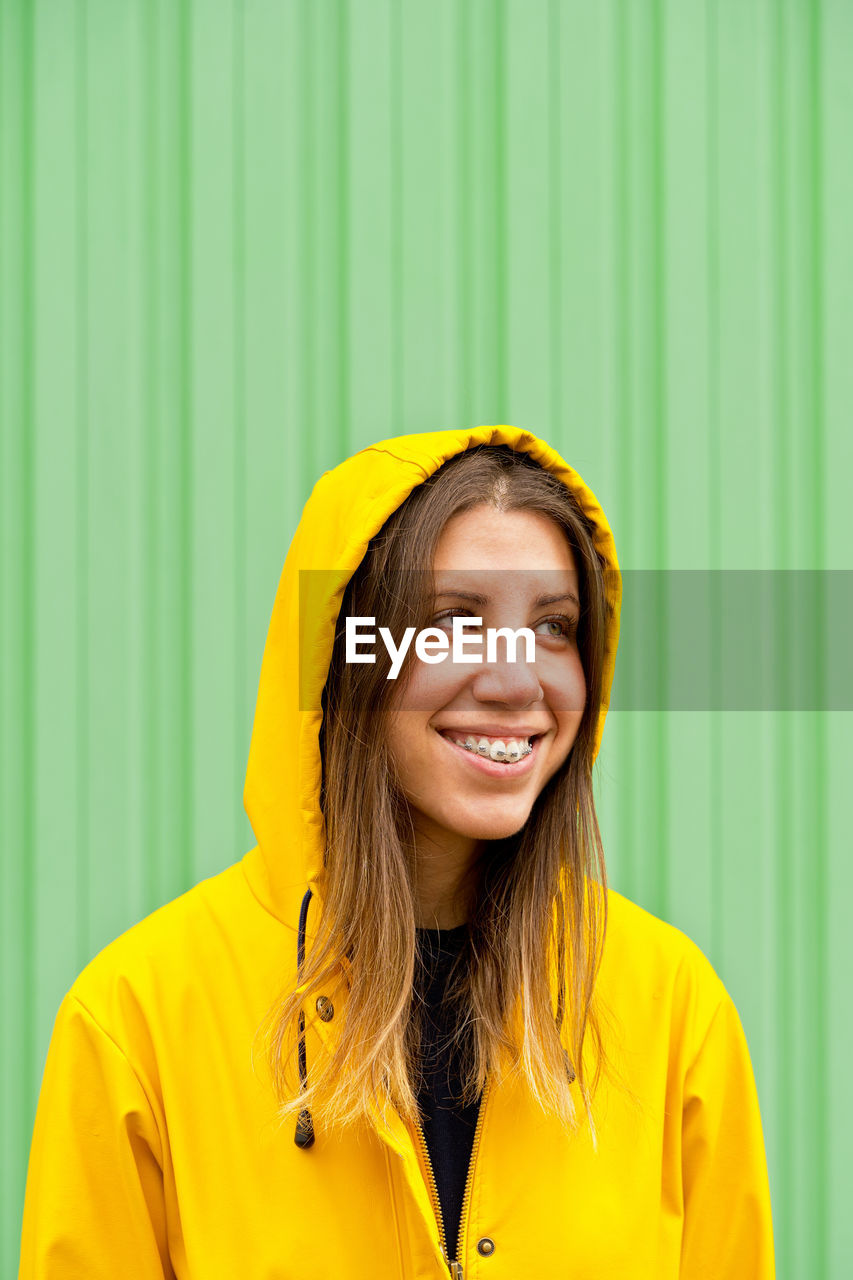 Young woman standing against green wall