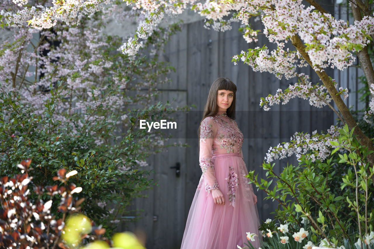 WOMAN STANDING BY PINK FLOWERING PLANT