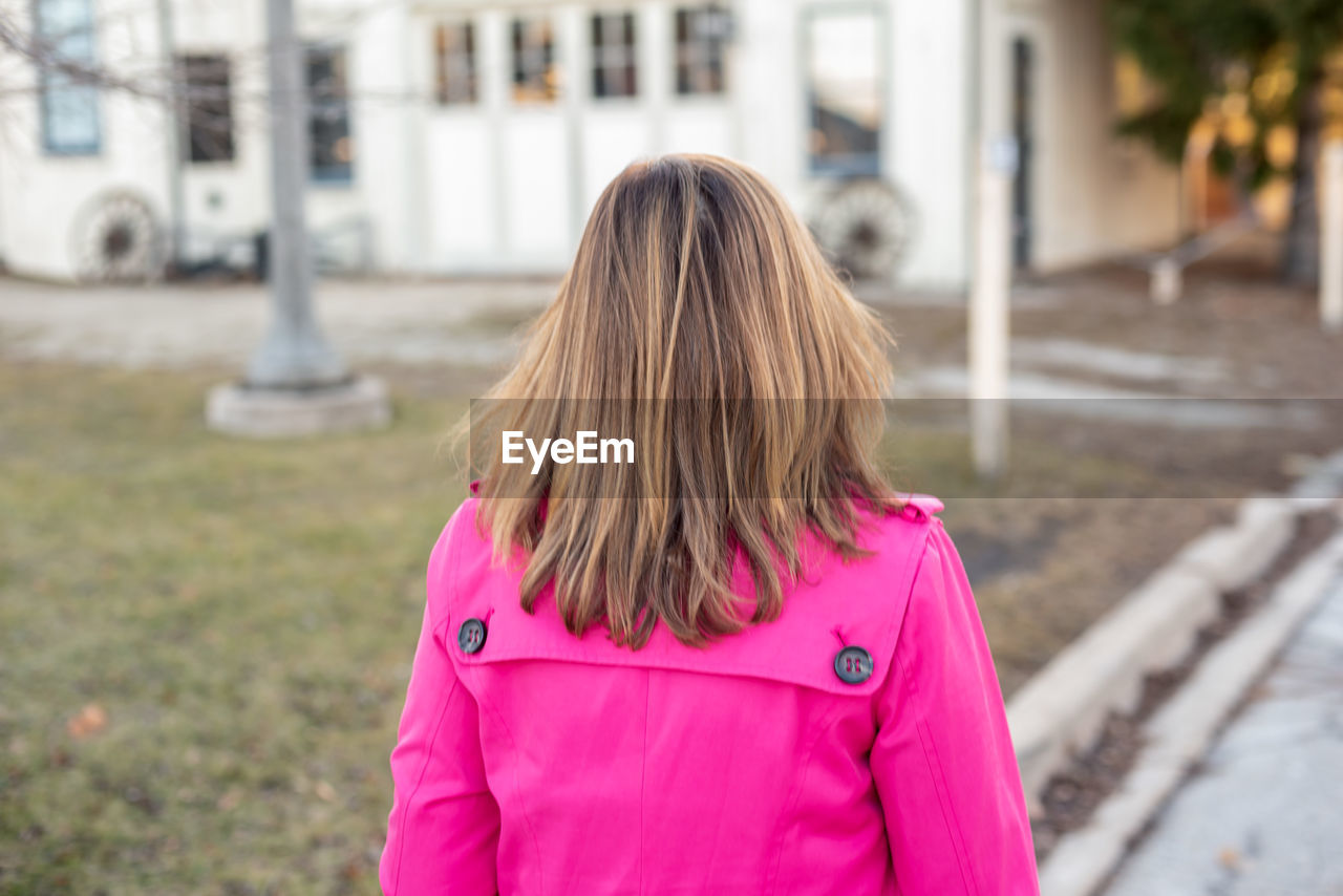 REAR VIEW OF WOMAN STANDING AGAINST PINK CITY IN BACKGROUND