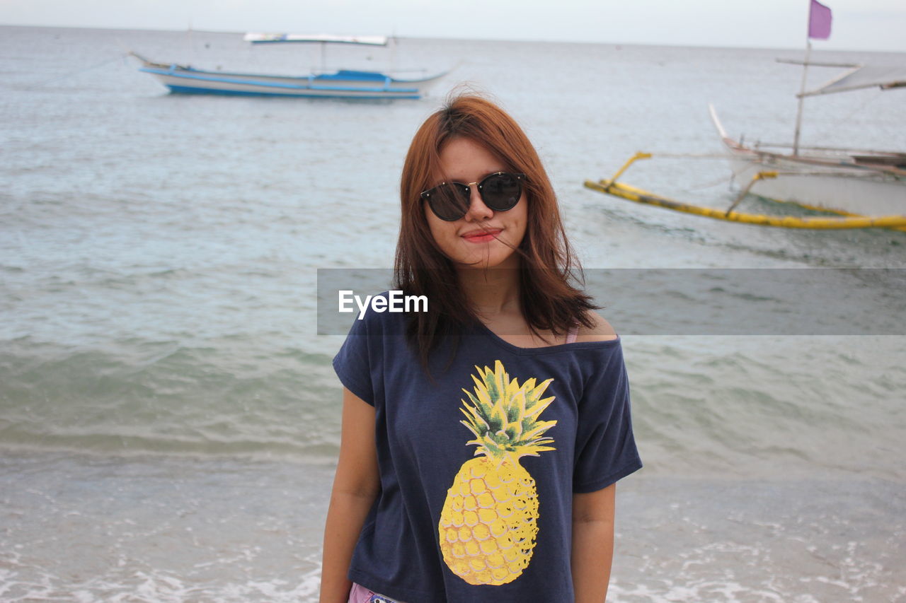 Young woman wearing sunglasses standing at sea shore