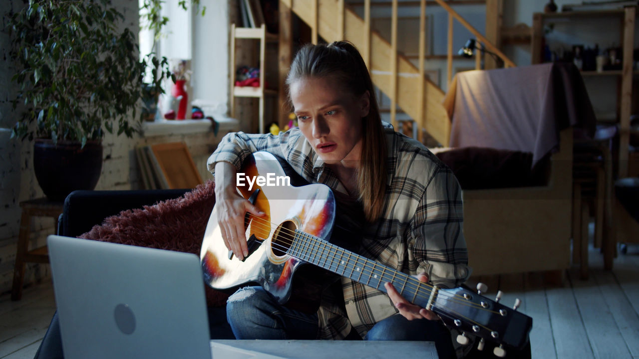 Woman learning guitar online at home