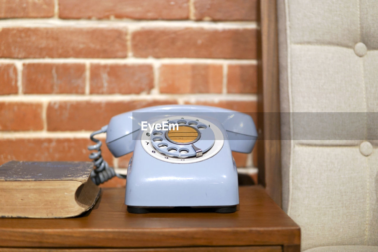 Vintage telephone on table against brick wall