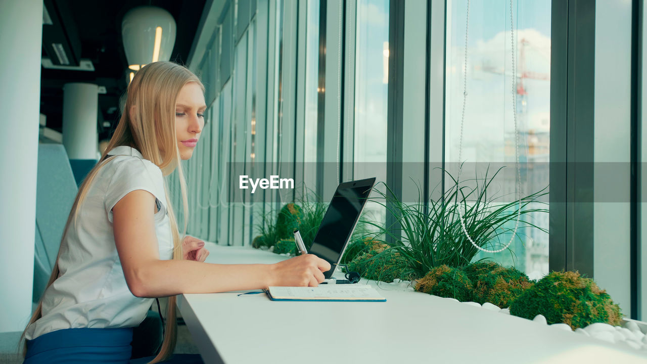 side view of woman using laptop while sitting on table