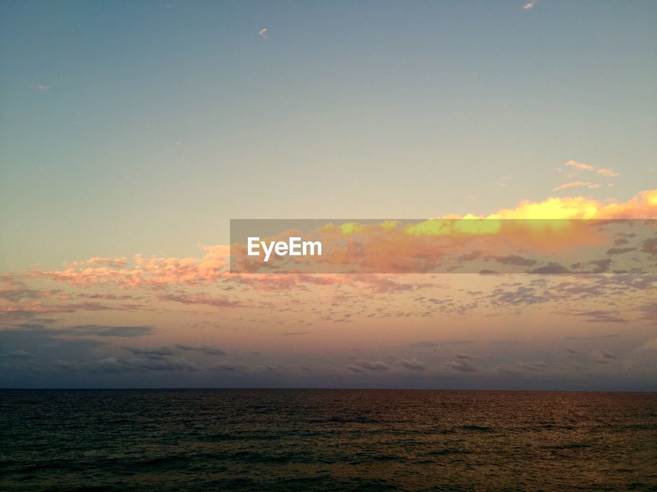 VIEW OF CALM SEA AGAINST DRAMATIC SKY DURING SUNSET