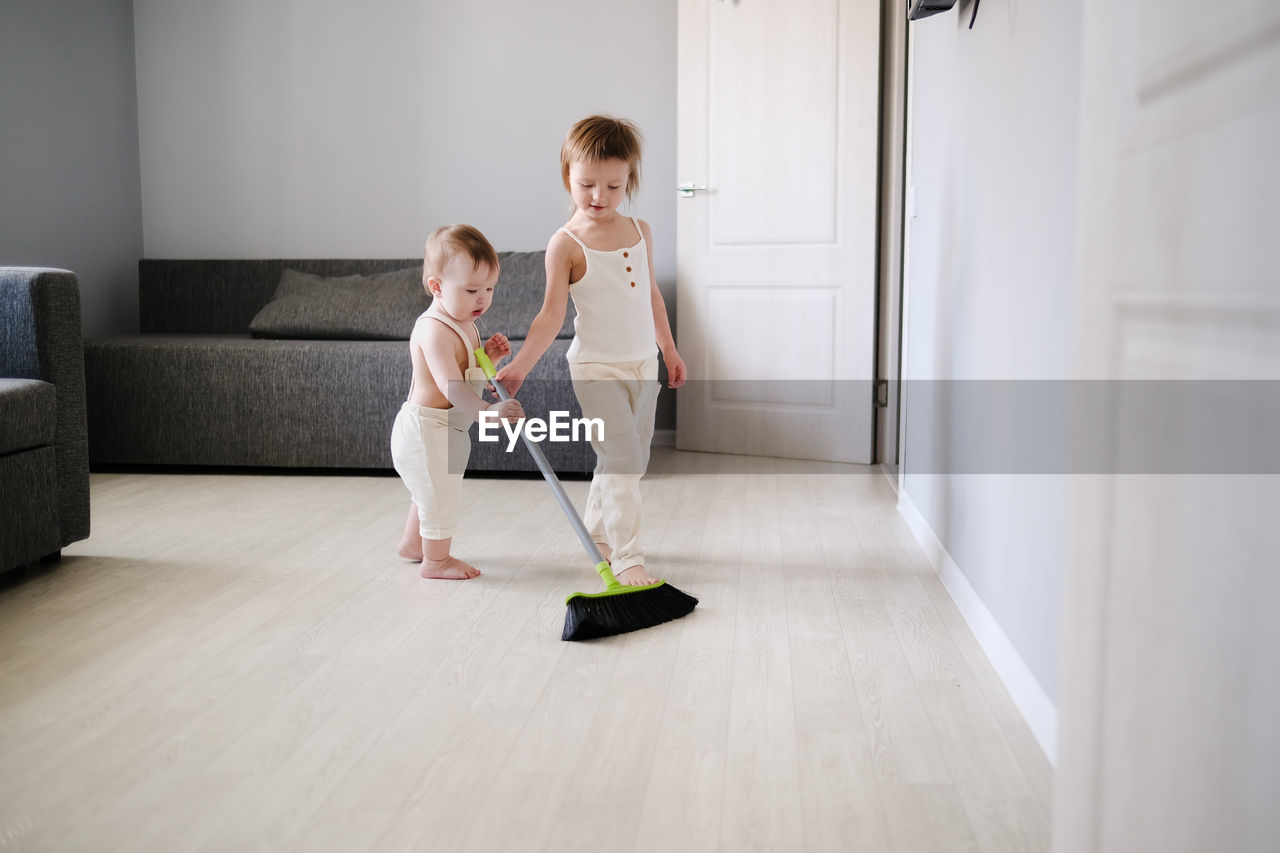 Children siblings with mop sweep floor in bright living room, help with housework and sibling 