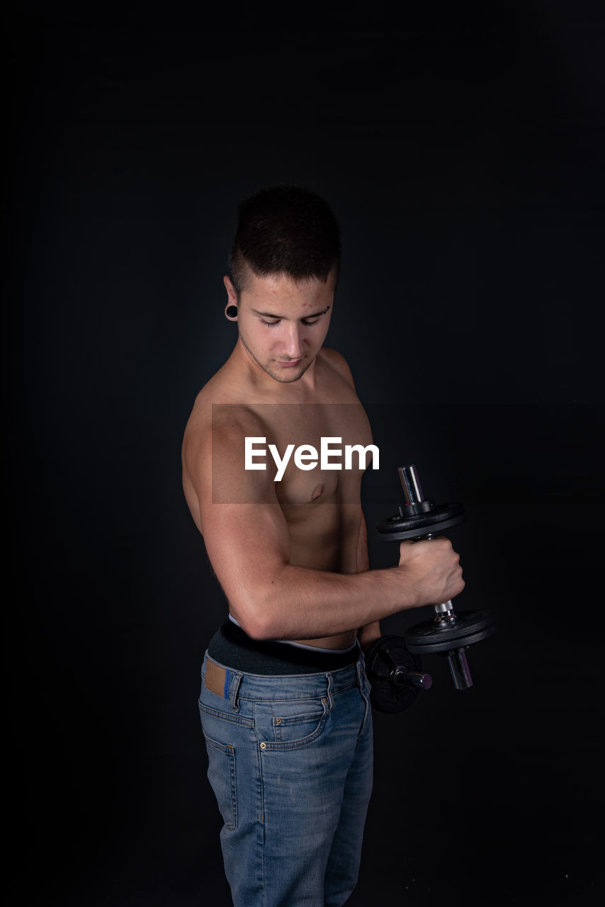 Shirtless man lifting dumbbells against black background