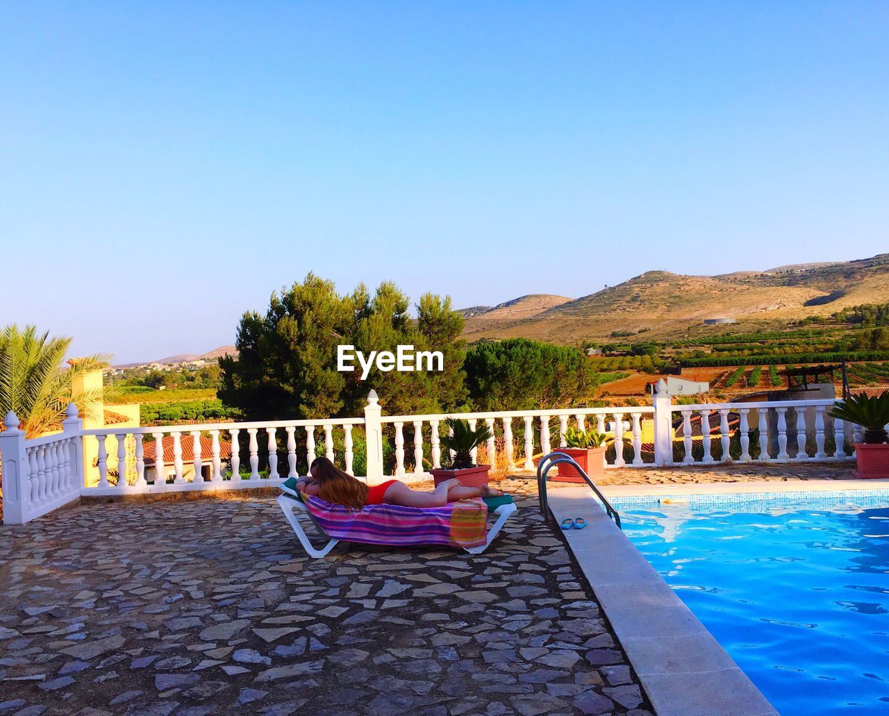 Woman relaxing on lounge chair by swimming pool against clear sky