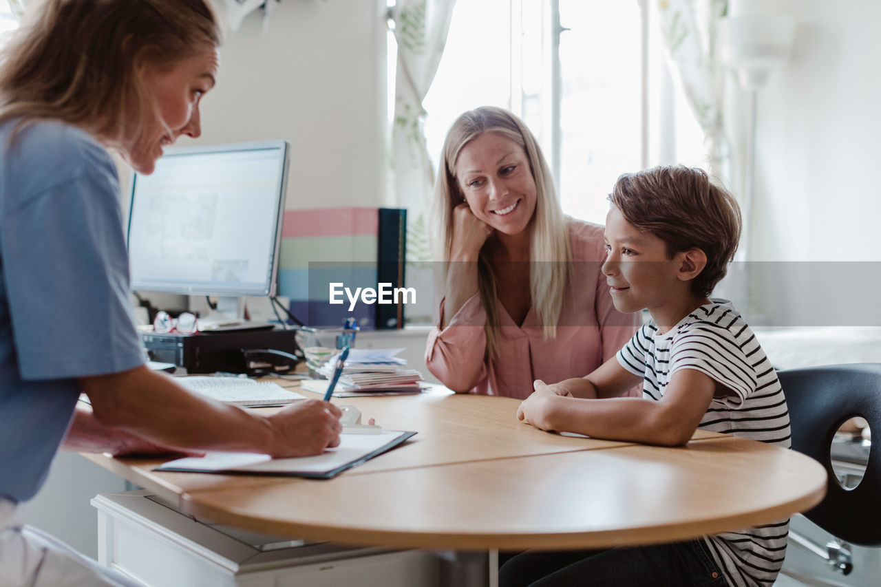 Mother and son consulting female pediatrician at desk in clinic