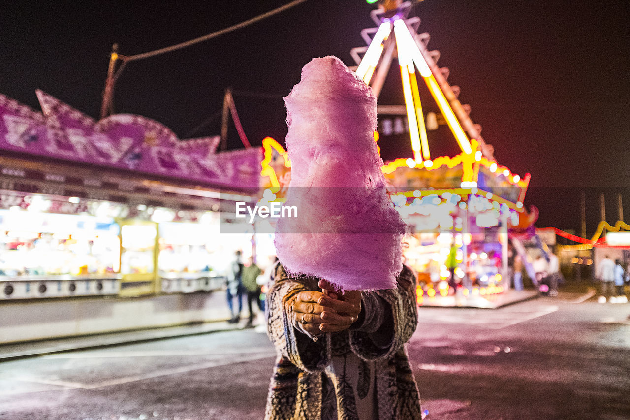 Woman holding cotton candy over face on land in city at night