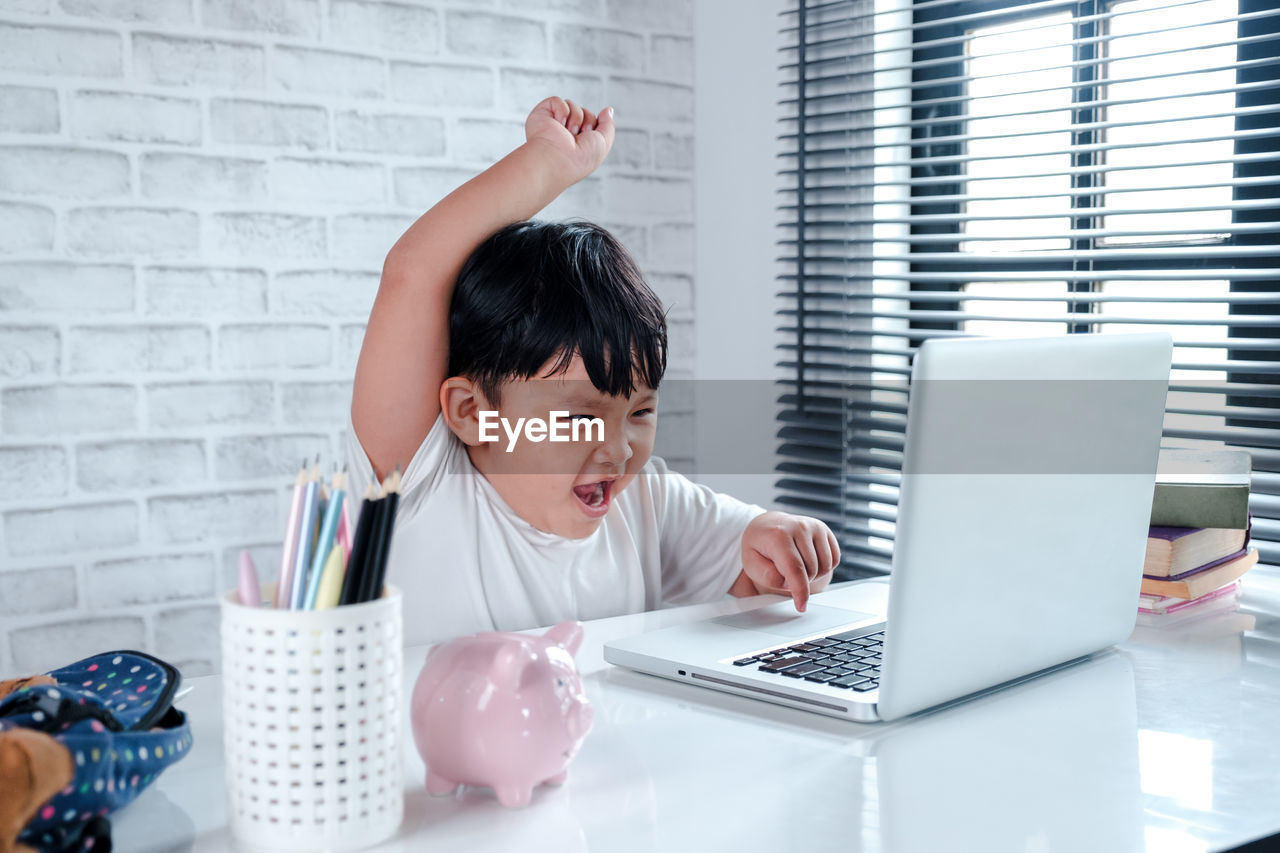 Boy celebrating success while using laptop on table