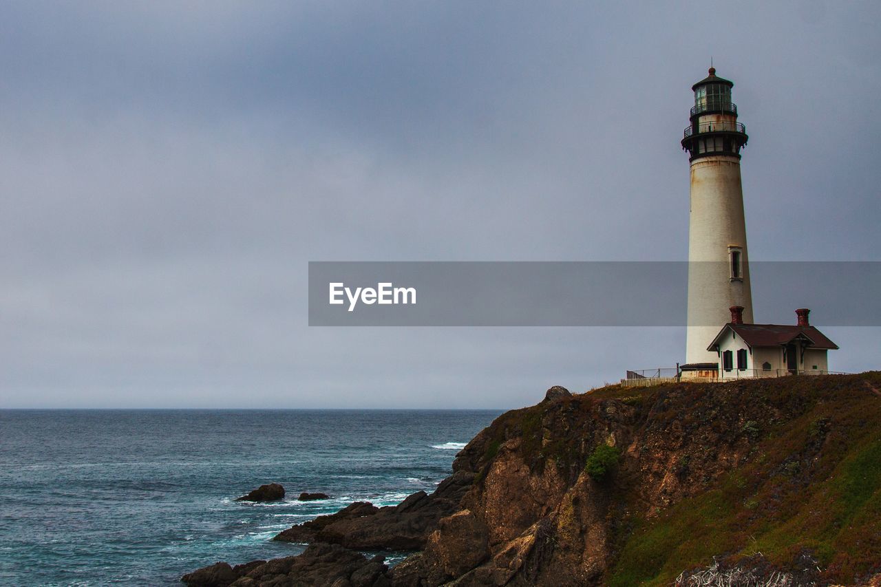 Lighthouse amidst sea and buildings against sky