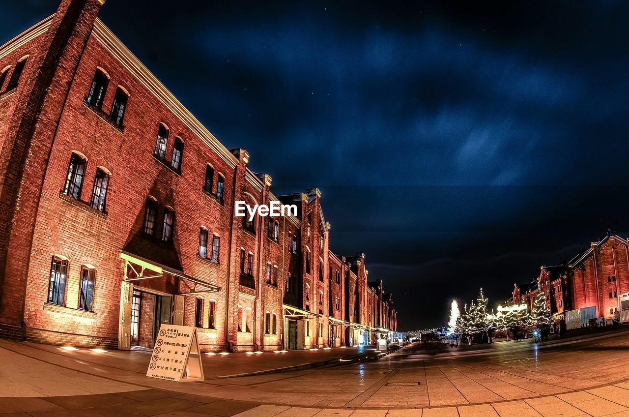 Illuminated buildings against cloudy sky at night