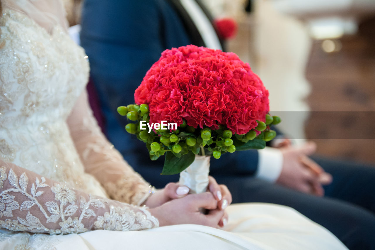 Midsection of bride and groom with carnation flower bouquet during wedding ceremony