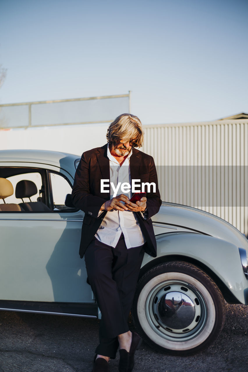 Senior man standing in front of vintage car using mobile phone