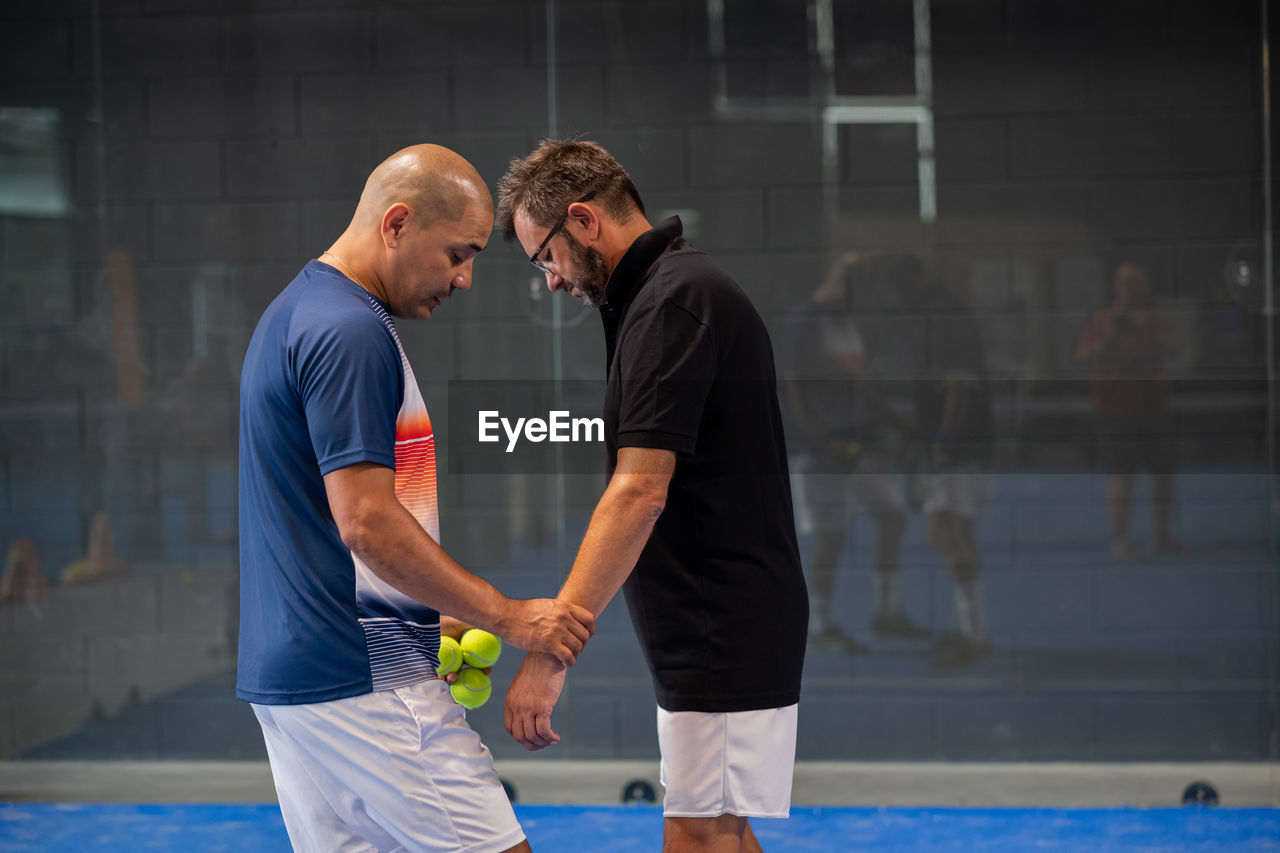 Monitor teaching padel class to man, his student - trainer teaches boy how to play padel 