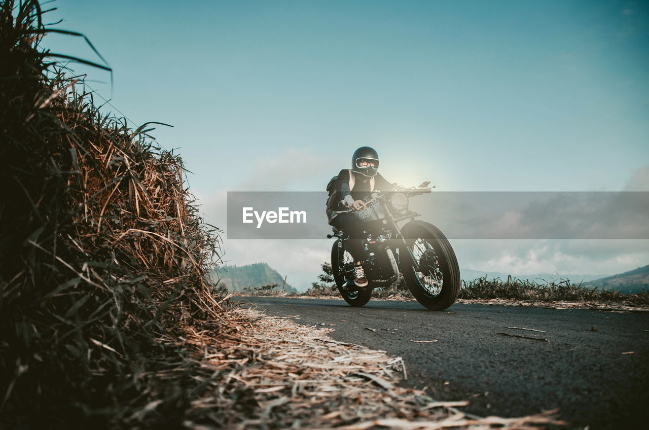 Man riding motorcycle on road against sky