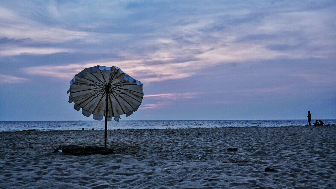 Umbrella at sandy beach against sky during sunset