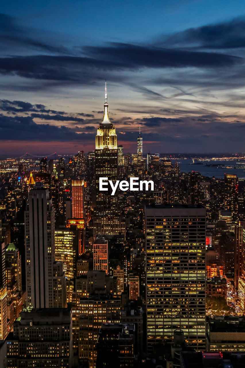 Illuminated empire state building amidst city against sky