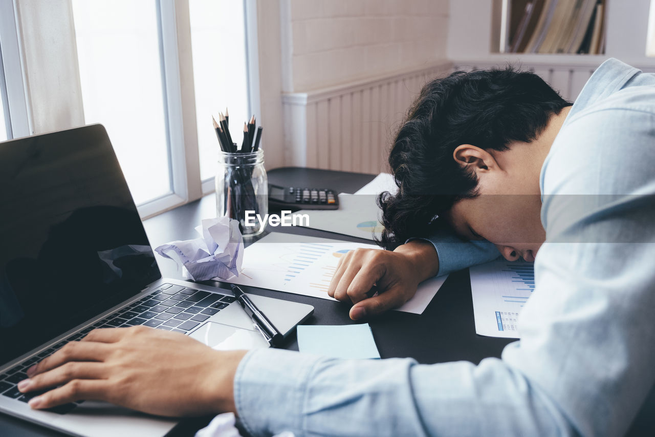 A young businessman who works hard and sleeps at his desk.