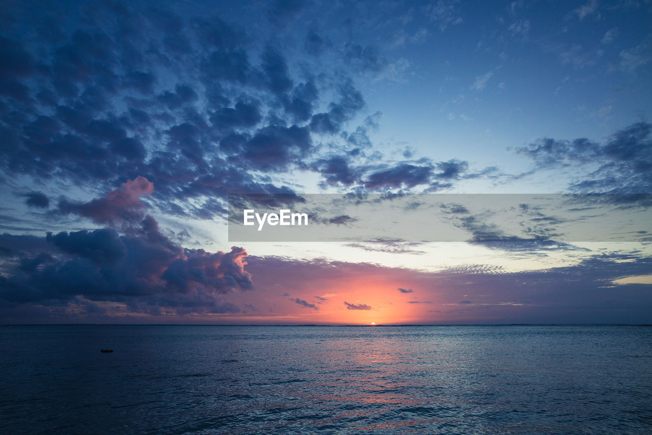 Scenic view of sea against cloudy sky during sunset