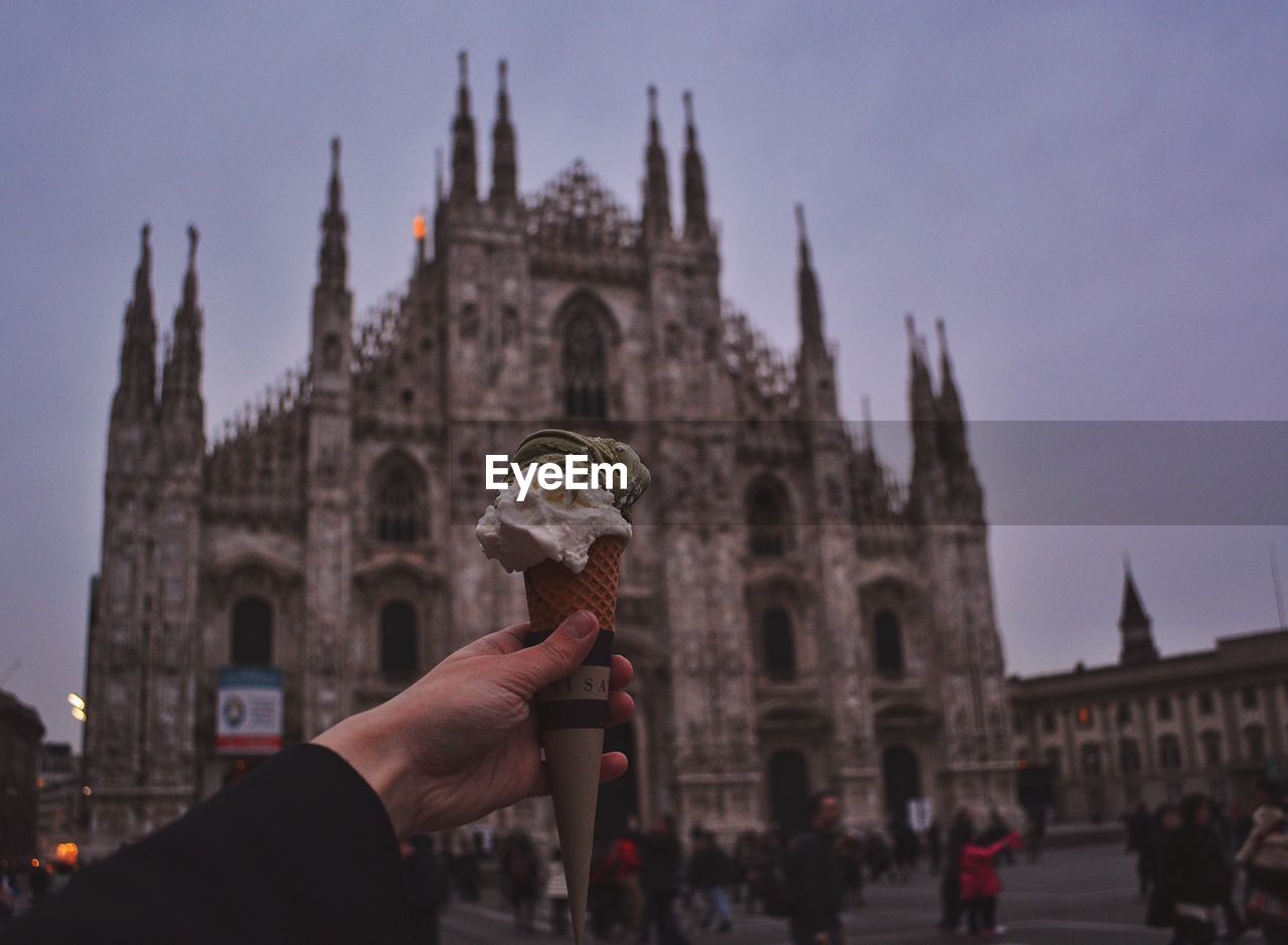 Cropped image of hand holding ice cream cone against duomo di milano