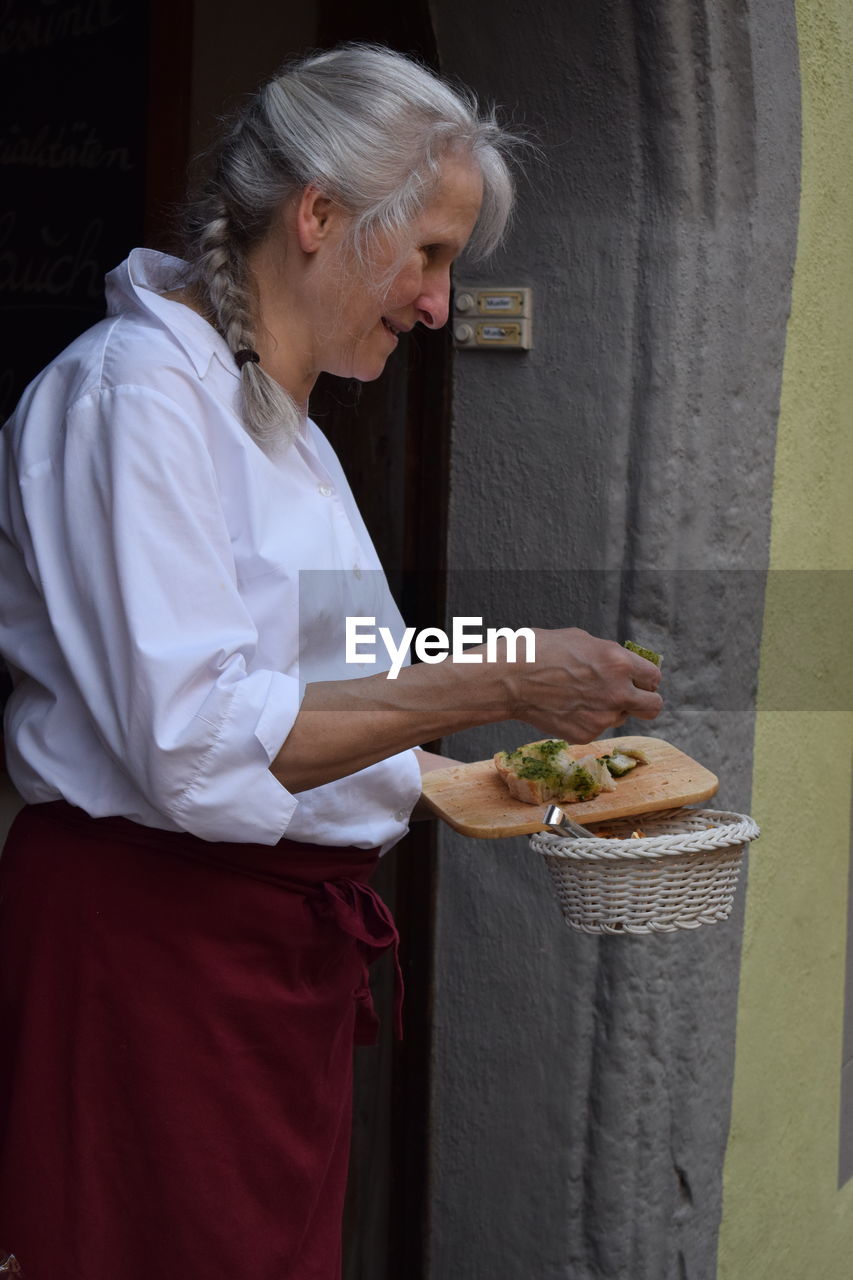 SIDE VIEW OF WOMAN HOLDING ICE CREAM STANDING AGAINST WALL