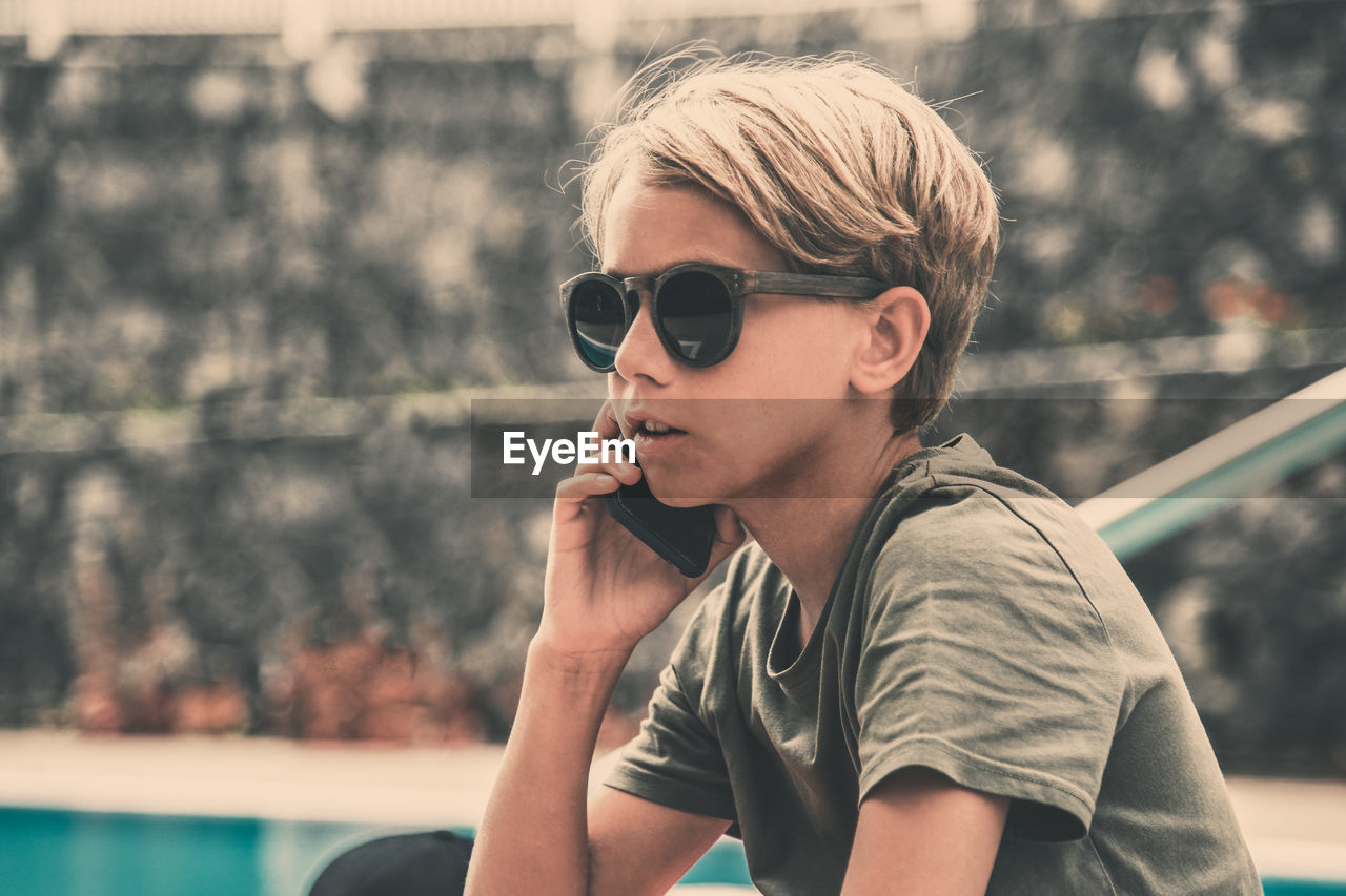 Boy wearing sunglasses talking on smart phone while sitting outdoors