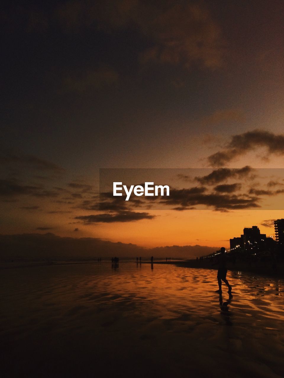 Silhouette man standing on shore at beach against sky during sunset