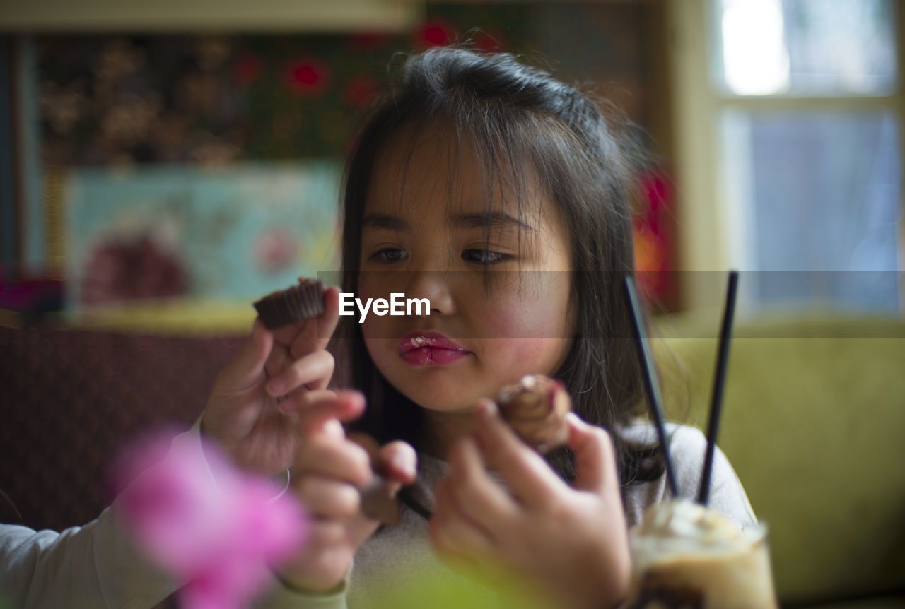 Cropped image of girl hand with sister eating cupcakes at home
