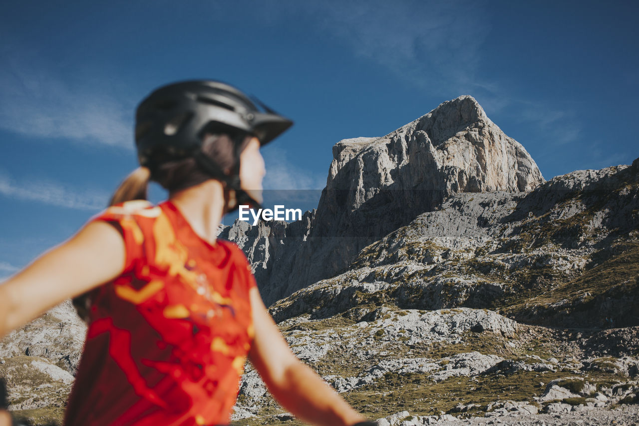 Female cyclist looking at rock mountain on sunny day, picos de europa national park, cantabria, spain