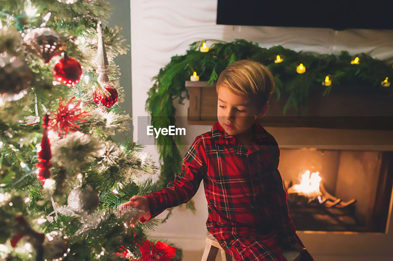 Boy hanging ornaments on christmas tree at night time