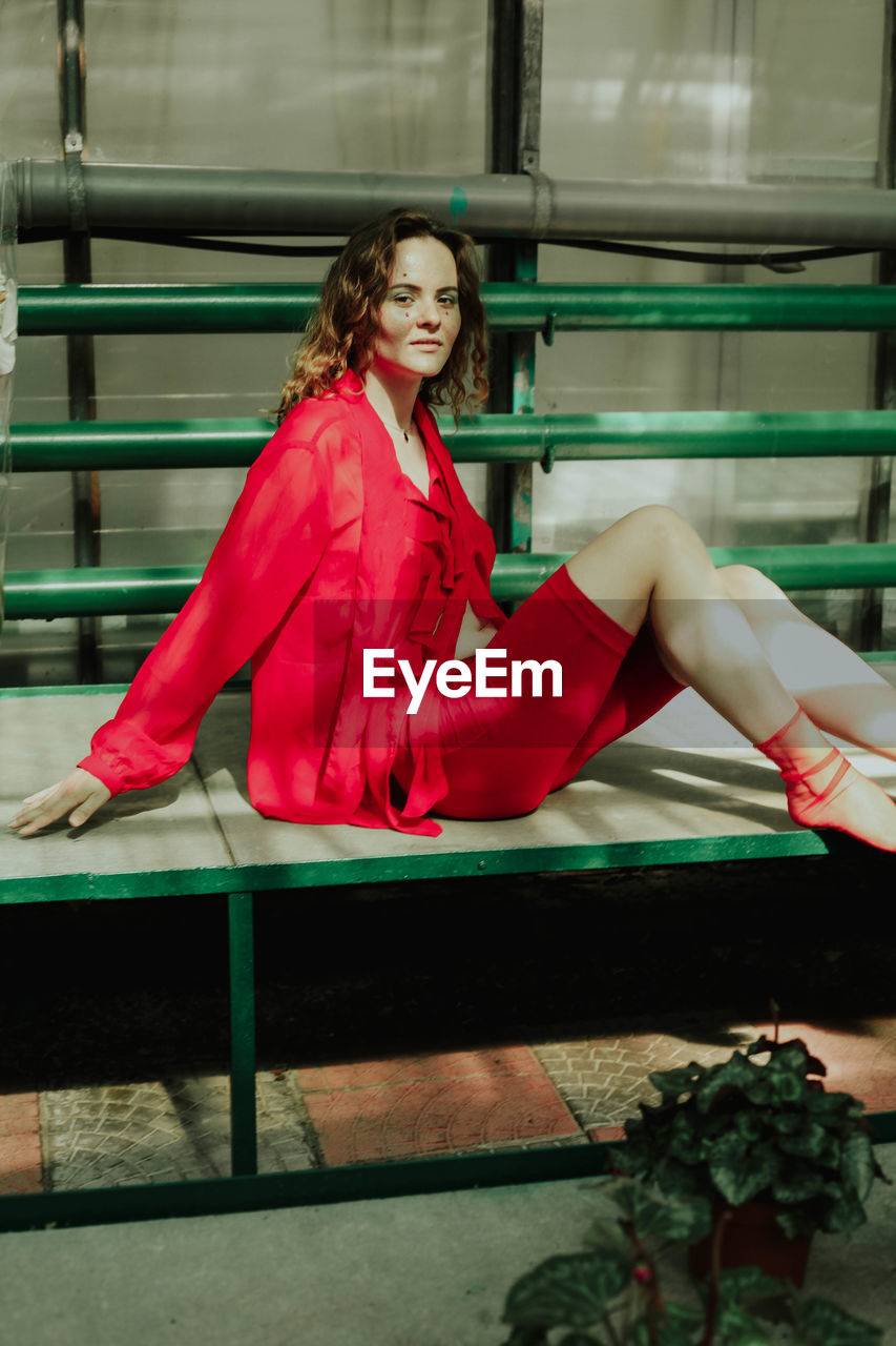 PORTRAIT OF YOUNG WOMAN SITTING ON RAILING