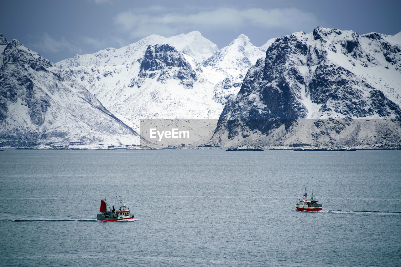 BOAT SAILING ON SEA AGAINST SNOWCAPPED MOUNTAINS