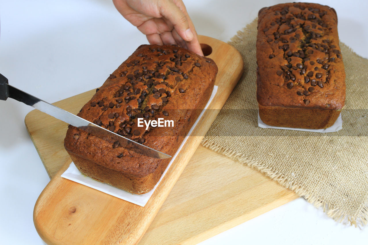 A lady's hand trying to cut the banana bread.