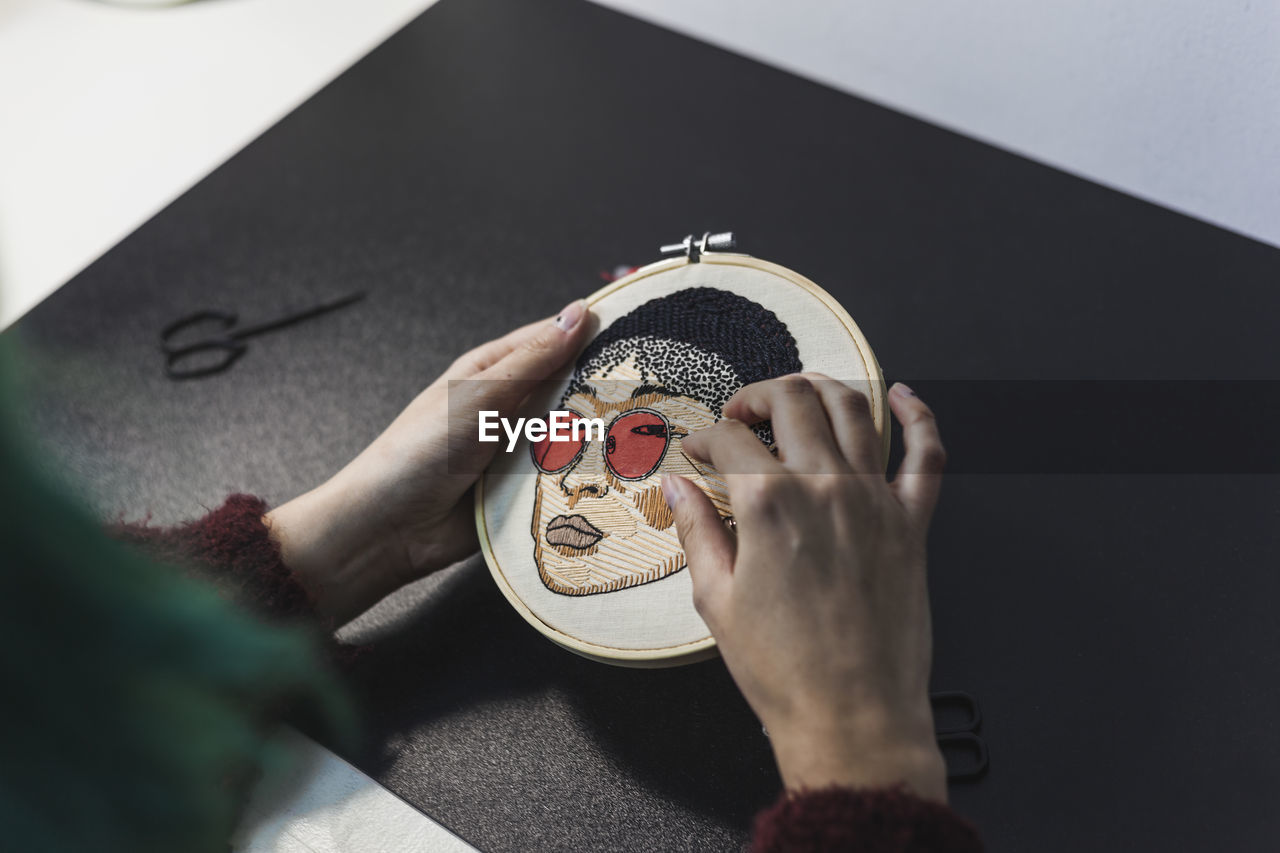 Hands of female craftsperson embroidering on cloth in frame at studio