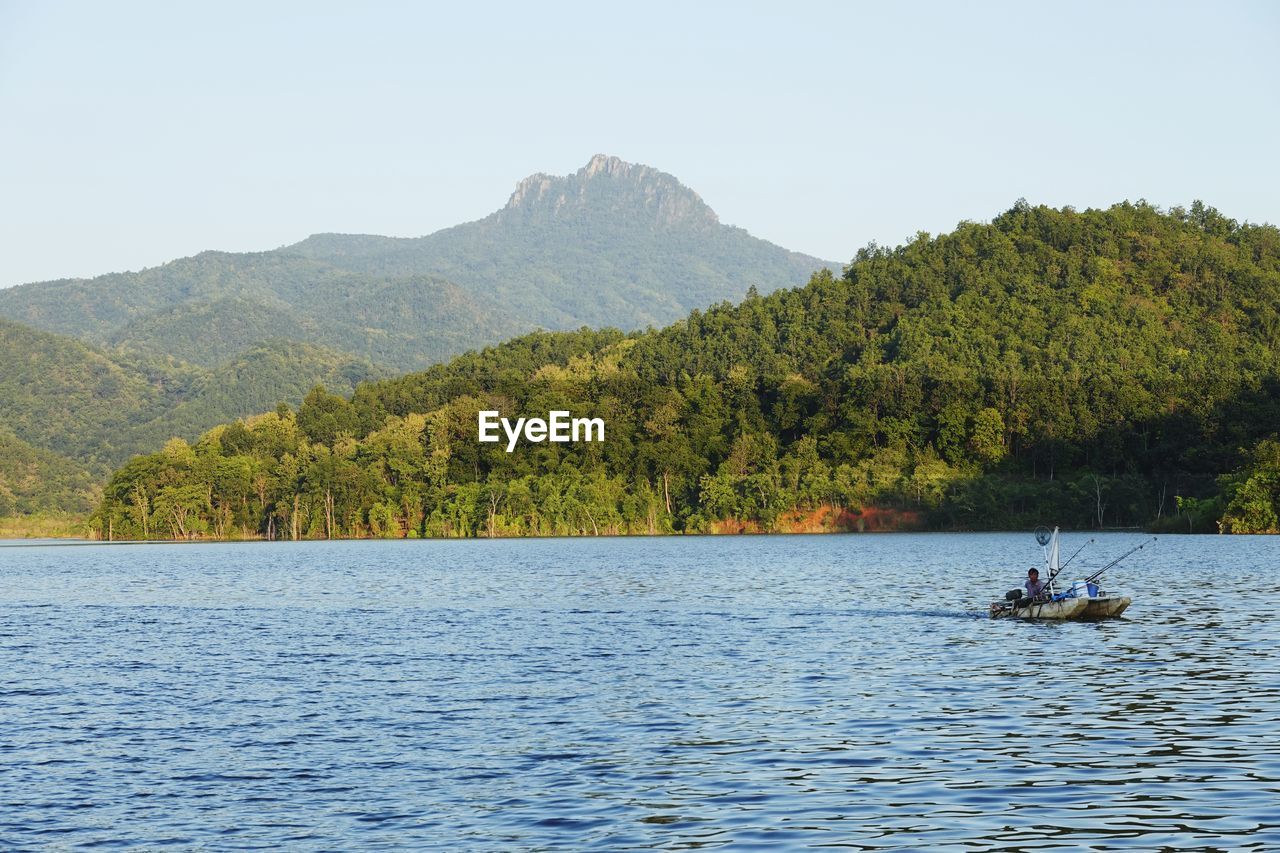 Mid adult man sitting in boat on lake against mountains