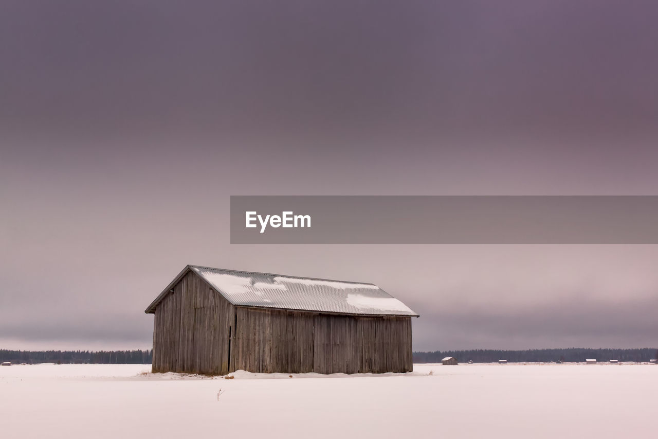 Barn on snowy landscape against sky