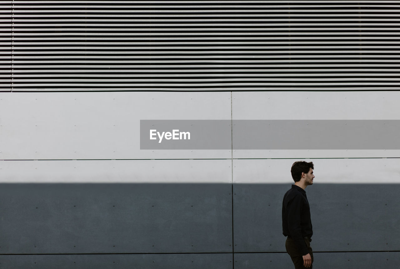 Young man looking away standing against wall