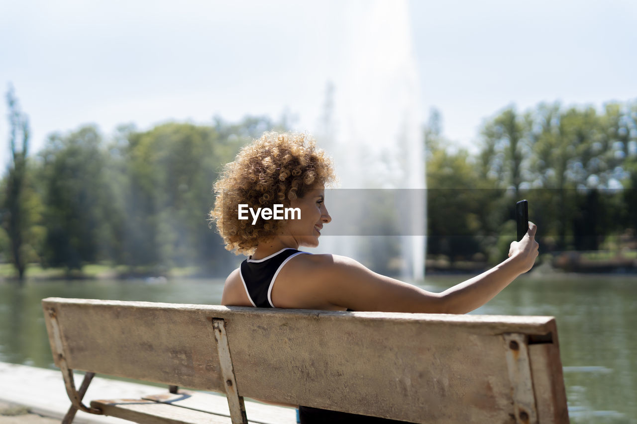 Woman on a bench by the lake taking a selfie