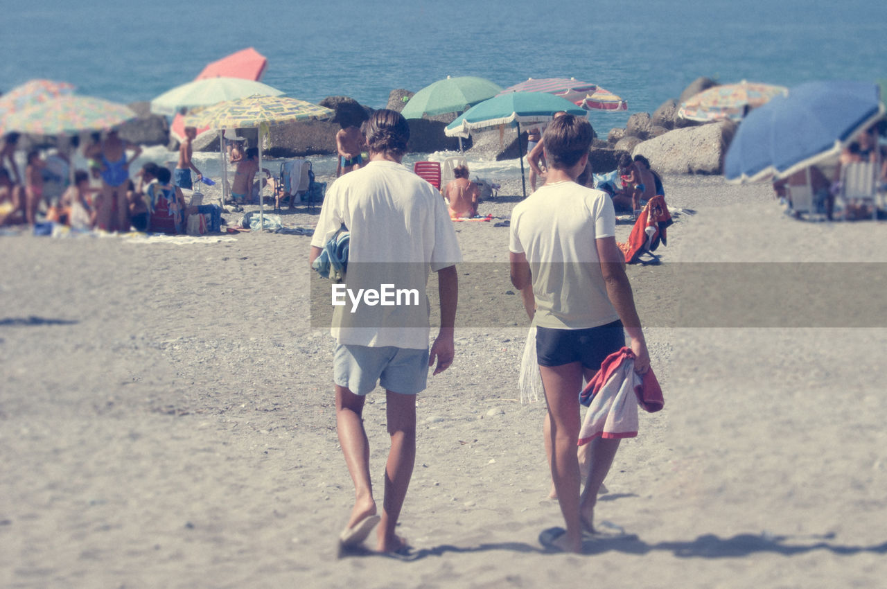 Rear view of men walking at beach