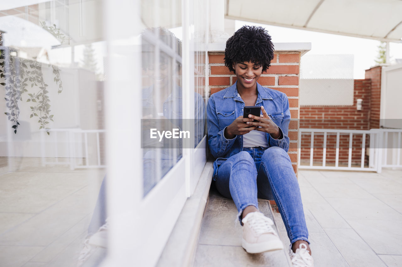 Happy woman using smart phone sitting on porch