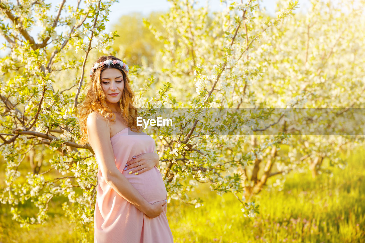 PORTRAIT OF SMILING YOUNG WOMAN STANDING BY YELLOW FLOWER