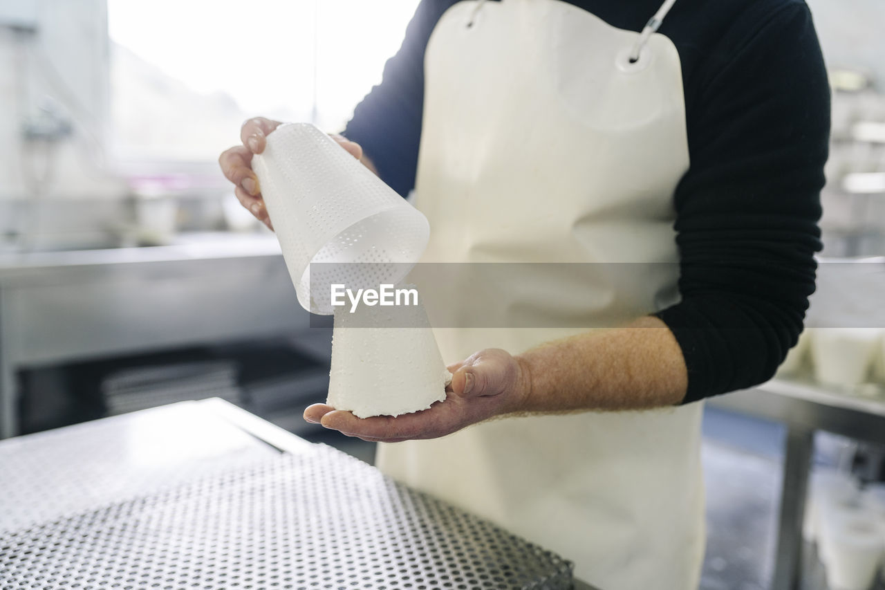 Mature male chef removing cheese from container in factory