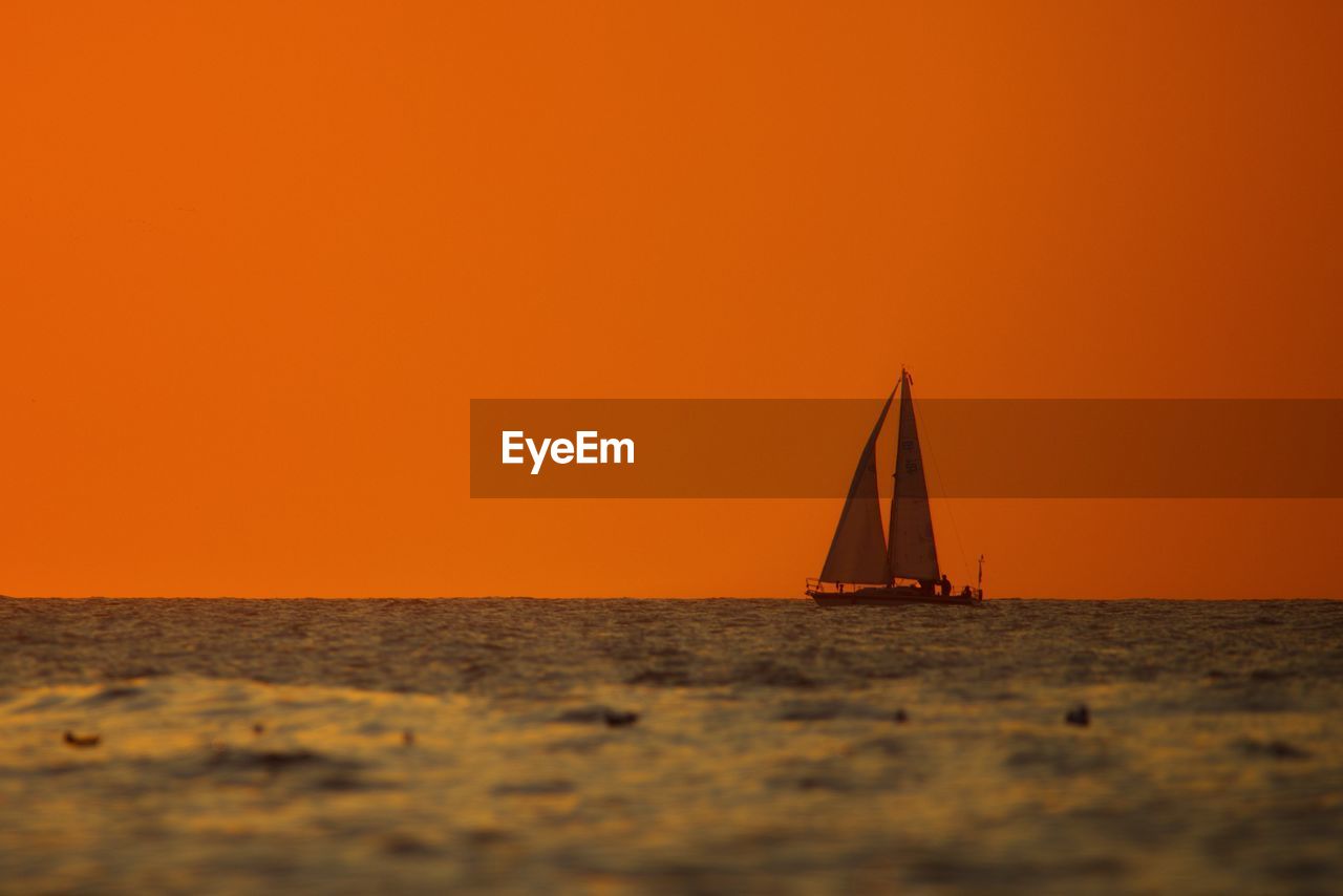 Sailboat sailing on sea against orange sky