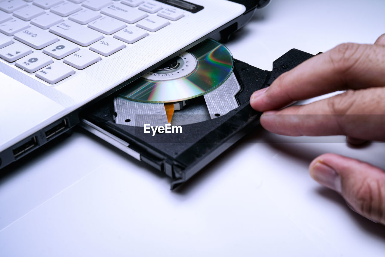 Close-up of hand inserting compact disc in laptop on table