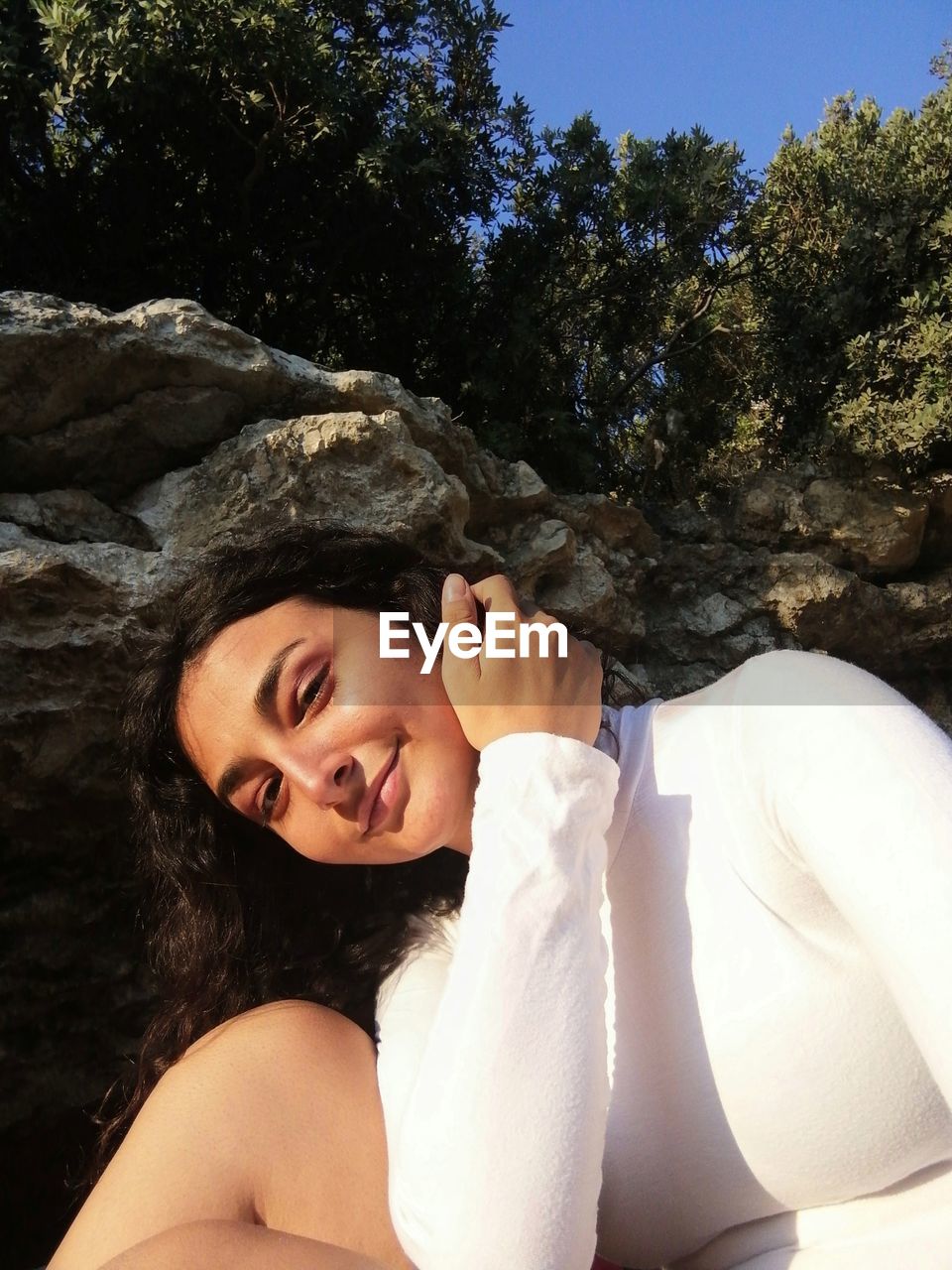 Portrait of smiling young woman sitting against rocks and trees